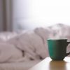Mug of steaming drink on a bedside table with an unmade bed blurred in the back