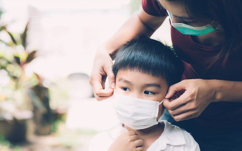 Mother putting a medical face mask on her son