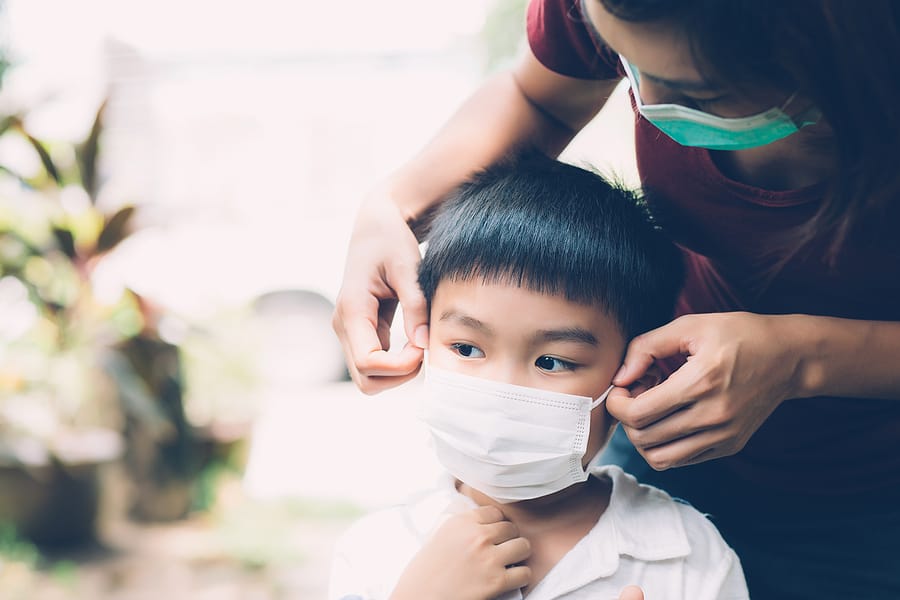 Mother putting a medical face mask on her son